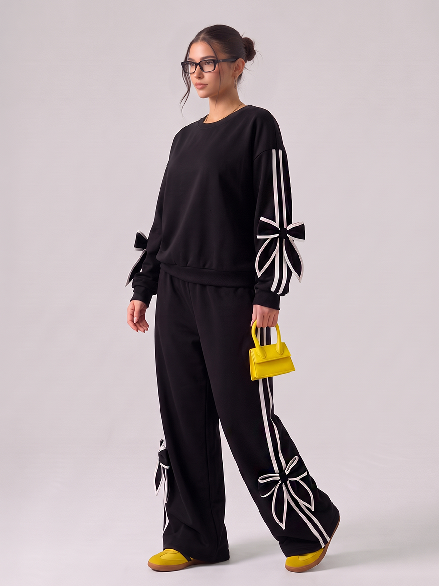 Woman wearing a black tracksuit with white bow details and side stripes