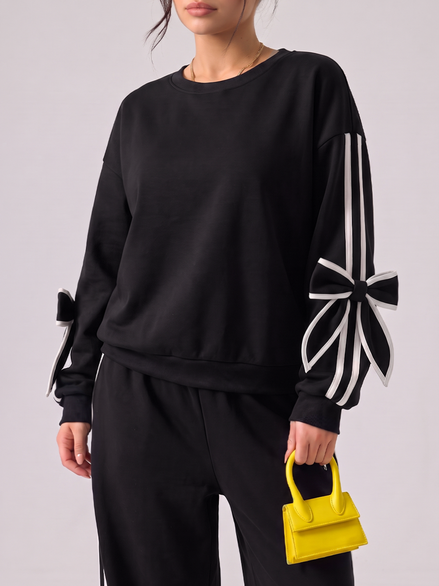 Woman wearing a black tracksuit with white bow details and side stripes