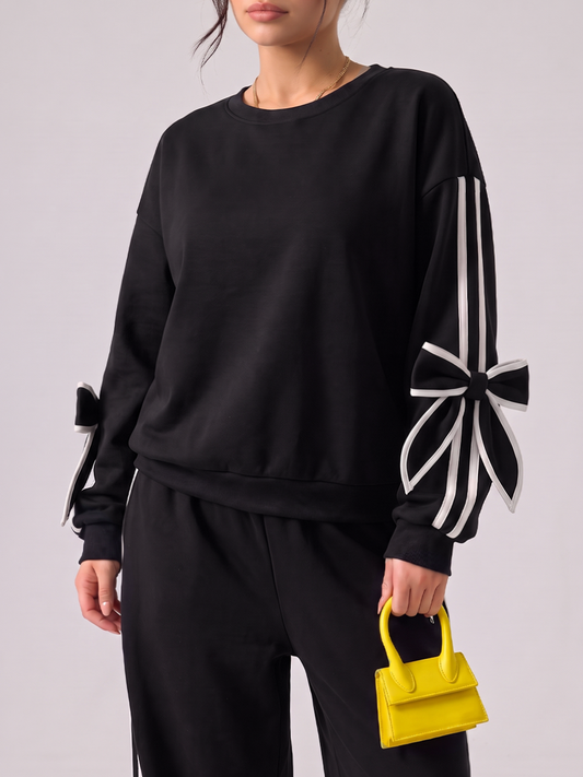 Woman wearing a black tracksuit with white bow details and side stripes