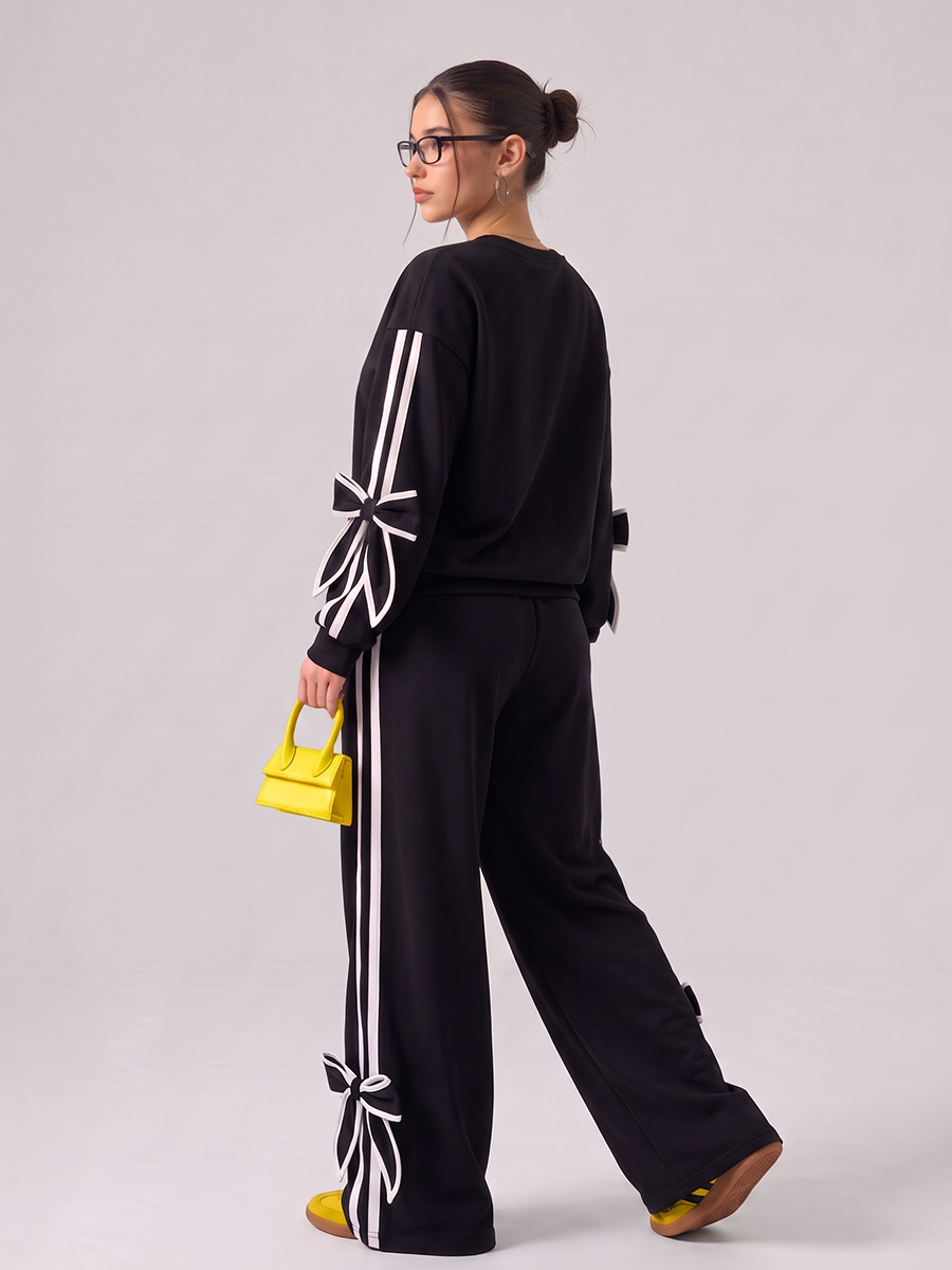 Woman wearing a black tracksuit with white bow details and side stripes